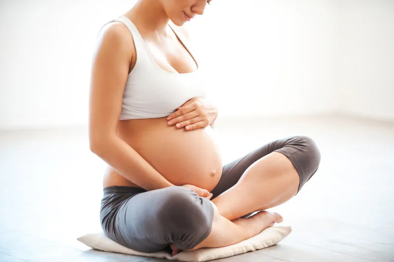 close-up of pregnant woman touching her belly while sitting in lotus position