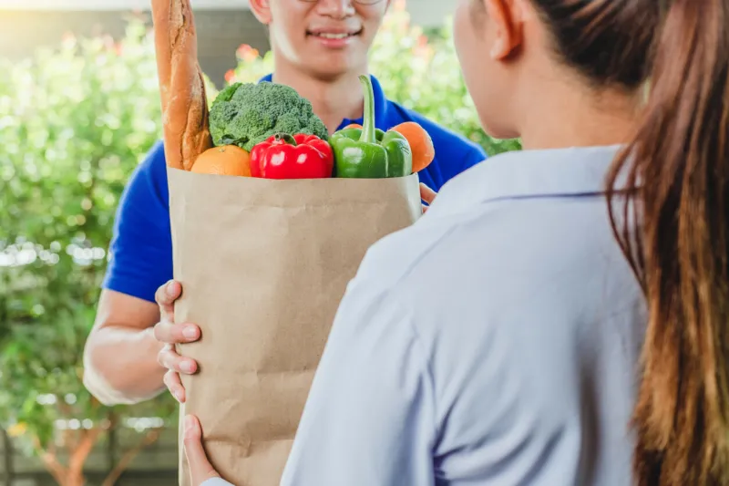 food delivery concept asian woman hand accepting bag of food, fruit, vegetable delivery from professional deliveryman postman and express grocery delivery