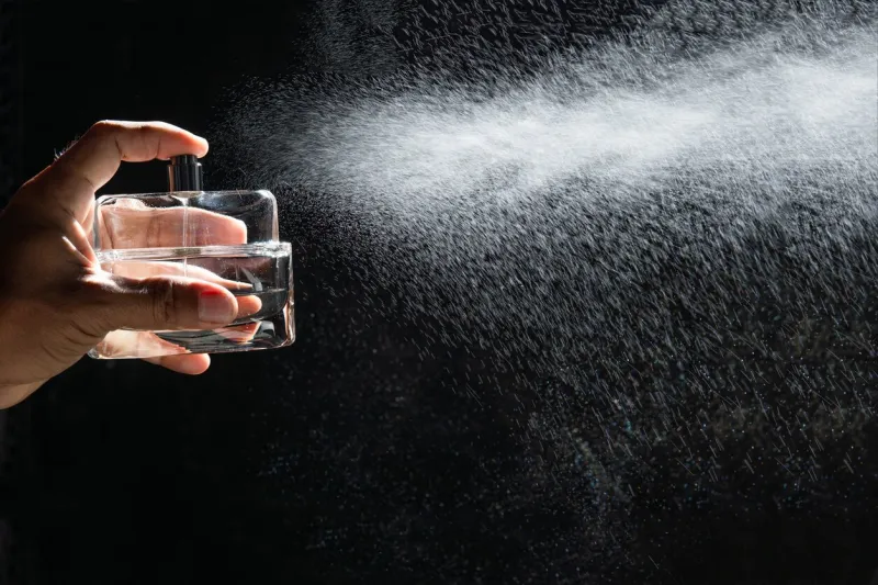 man spraying perfume on dark background, closeup