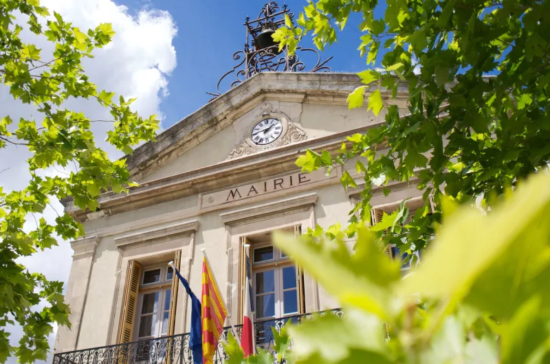 scenic hotel de ville in provence, france, blue sky, flags, green trees
