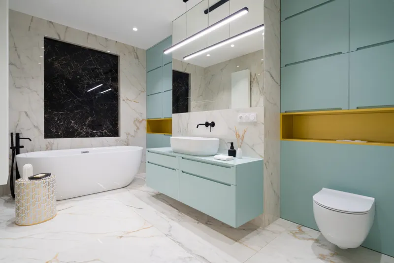 spacious and modern bathroom with oval bathtub, toilet, washbasin, new designed blue and gold furniture and marble floor and wall tiles