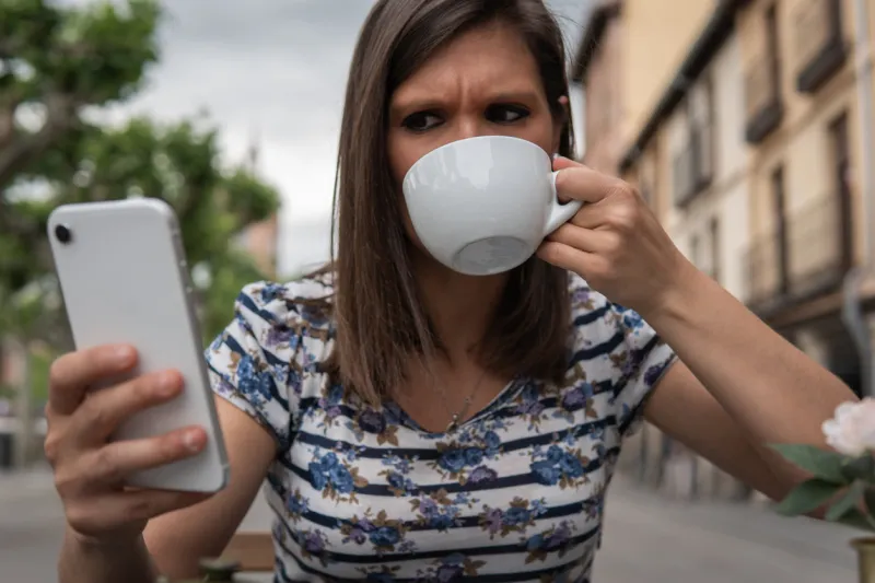 young woman looking sideways at her phone terminal while she sips her drink lifestyle concept