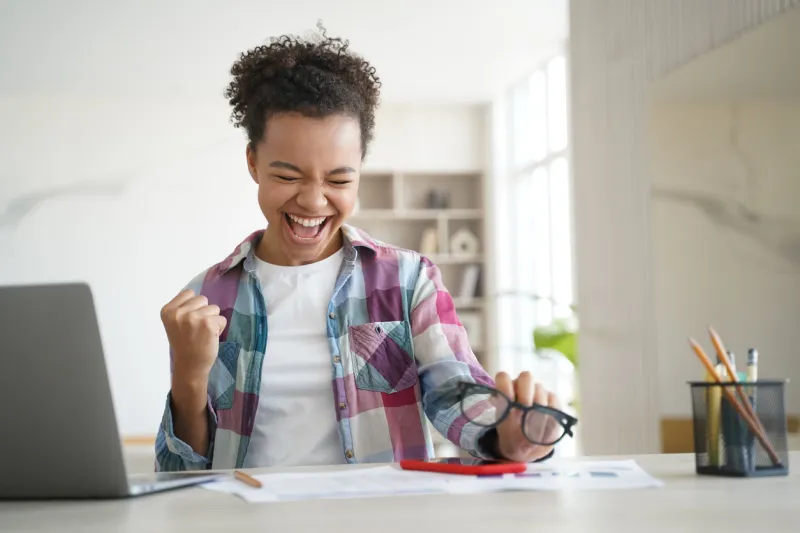 excited happy african american high school girl, celebrating victory, got email with good exam test scores overjoyed biracial teen student got good news online sitting at laptop distance education