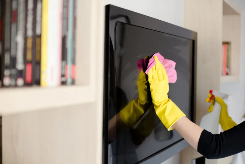 woman in yellow rubber gloves cleaning tv with pink cloth