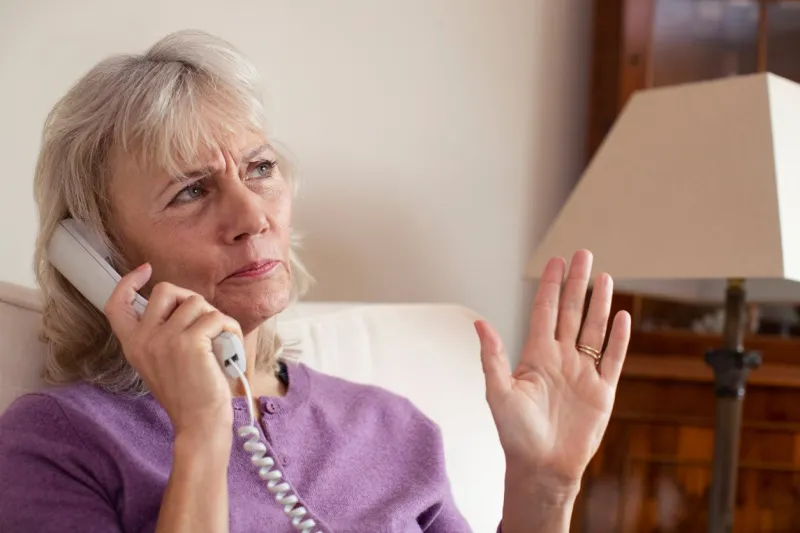 senior woman receiving unwanted telephone call at home
