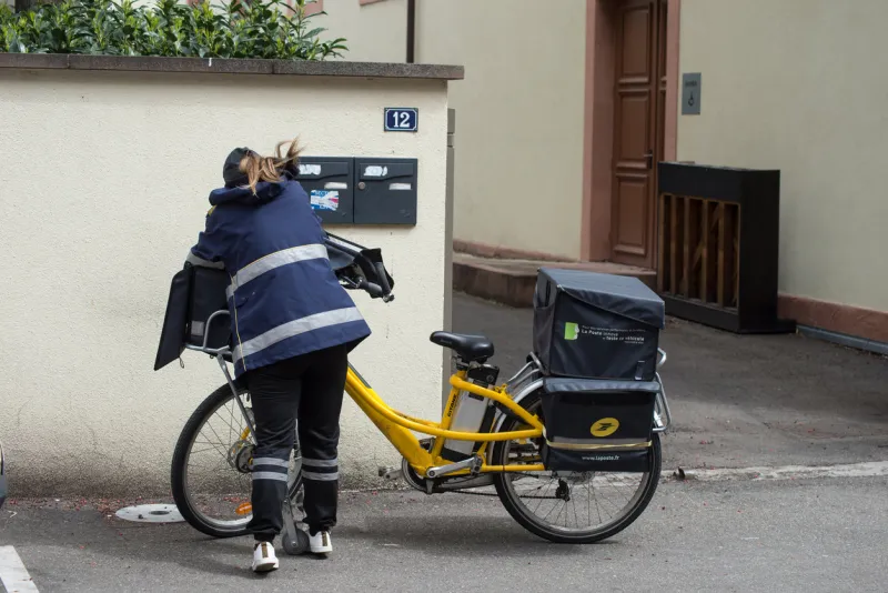 mulhouse - france - 4 may 2021 - portrait of postwoman putting letters in mail boxes in the street