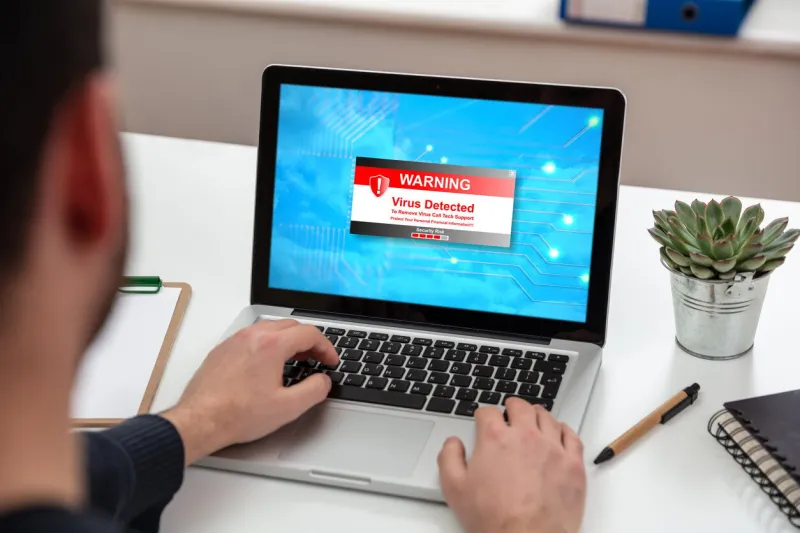 virus detected warning message on computer screen, cyber attack concept man working on a laptop, office business wood desk background