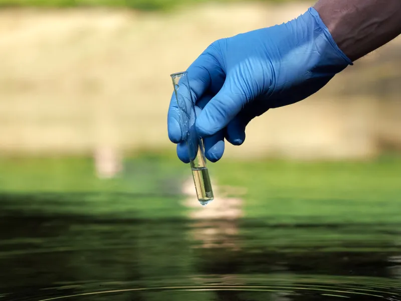 water sample hand in glove holding a test tube of clear water concept - water purity analysis, environment, ecology water testing for infections, permission to swim