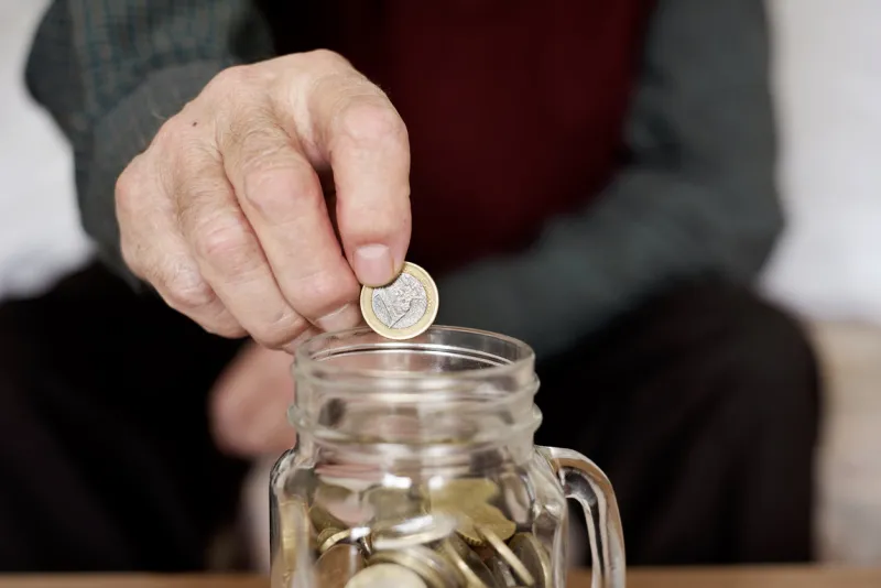 closeup of an old caucasian man saving a one euro coin in a glass pot
