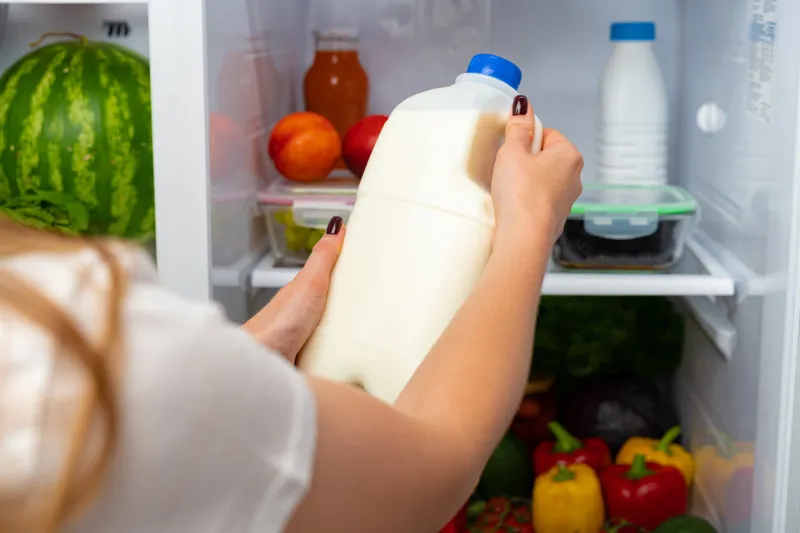female hand taking bottle of milk from a fridge close up