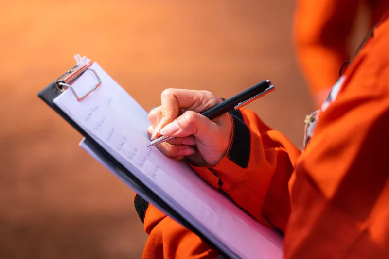 safety officer supervisor is writing note on the checklist paper during perform audit and inspection in oil field operation close-up action and selective focus photo
