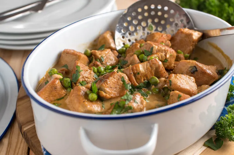 delicious homemade cooked chicken ragout or chicken goulash with a tasty cream sauce and green peas served in a rustic stew pot on wooden table ready to eat