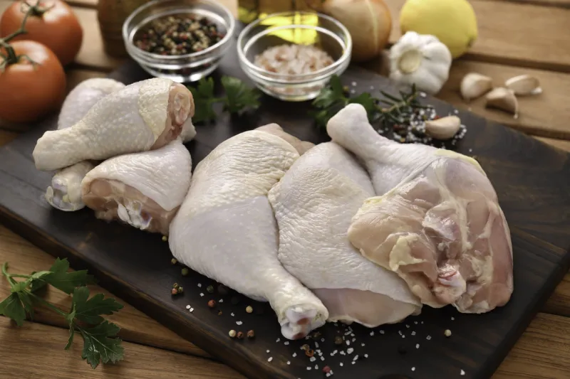 fresh raw chicken thighs with ingredients for cooking on a wooden cutting board