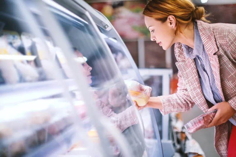 attractive smiling brunette taking meat from a fridge at local supermarket side view horizontal