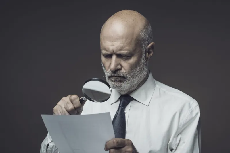 businessman checking a document using a magnifier, contracts and agreements concept