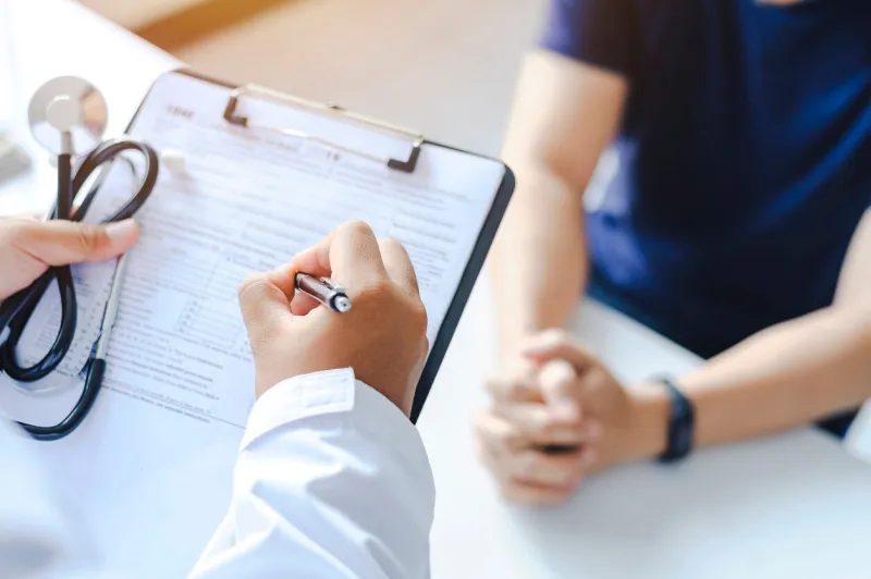 close-up of a male doctor hand hold a silver pen and showing pad in hospital doctor giving prescription to the patient and filling up medical form at a clipboard