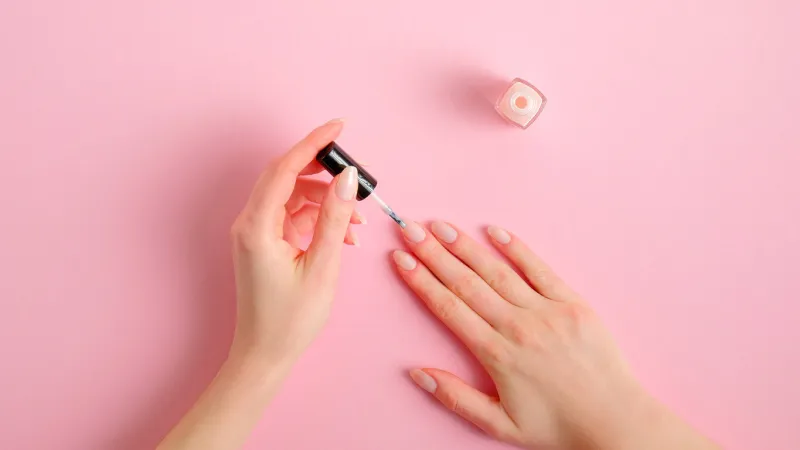 woman applying polish on nails at home female hands with elegant manicure and nail polish bottle on pink background, top view beauty treatment and hand care concept