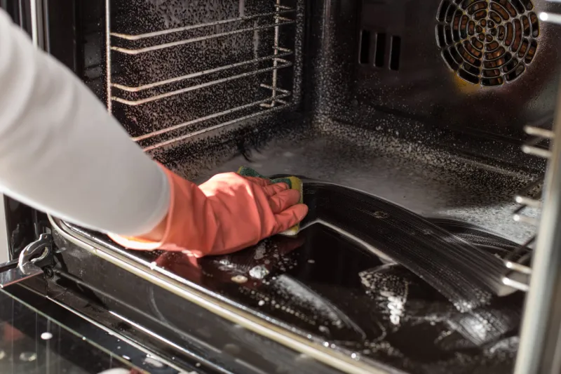 close up of female hands with protective gloves scrubbing oven in kitchen