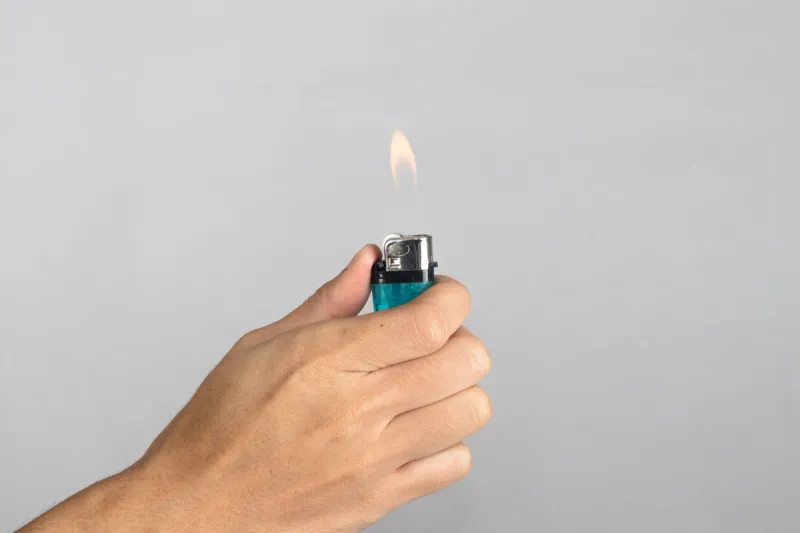 hand holds blue lighter in hand and pressing it isolated on whi