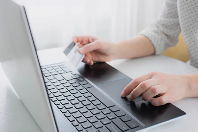 woman's hands holding credit bank card and using laptop computer at home online shopping concept