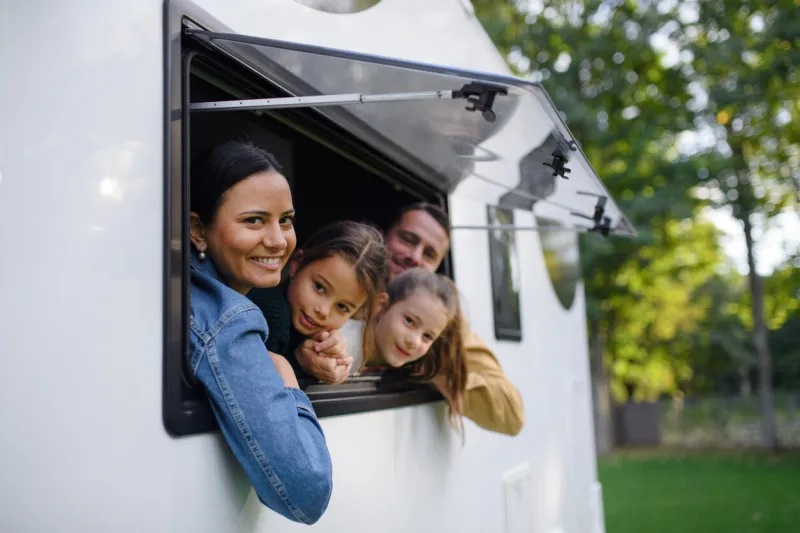 a happy young family with two children looking out of caravan window