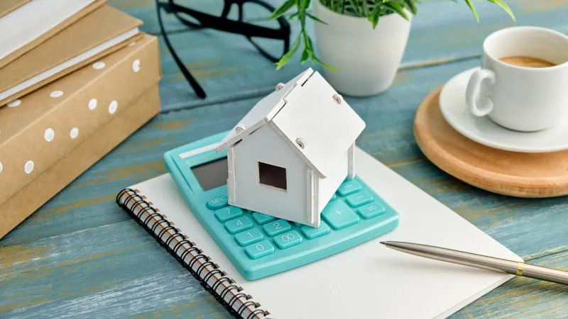 model house with a calculator on wood desk on wood background