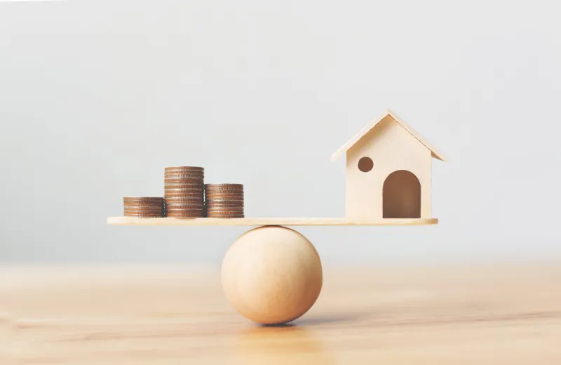 wooden home and money coins stack on wood scale property investment and house mortgage financial real estate concept