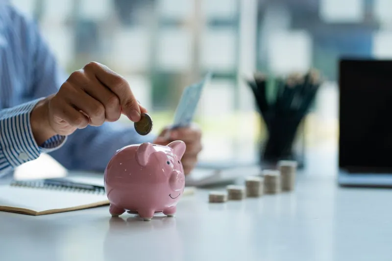 hands of a young asian businessman man putting coins into piggy bank and holding money side by side to save expenses a savings plan that provides enough of his income for payments