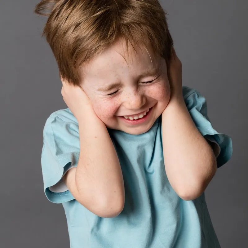 fragile little child closing his ears and eyes against domestic violence or education, having problems with his parents, grey background