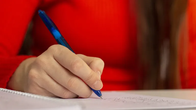 a girl at the table writes with a pen in a notebook student studying, taking notes school and education closeup photo