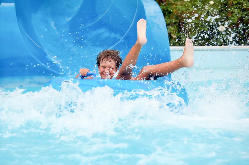 happy an 8 year old boy is riding in the water park on inflatable circles on water slides with splash