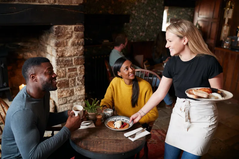 waitress working in traditional english pub serving breakfast to guests