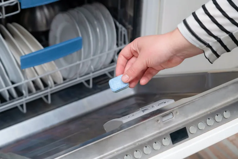 close up of hand inserting soap capsule into dish washer in the kitchen person putting dish washing detergent into machine