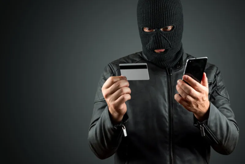 robber, a thug in a balaclava holds a credit card in his hands on a dark background robbery, hacker, crime, theft copy space
