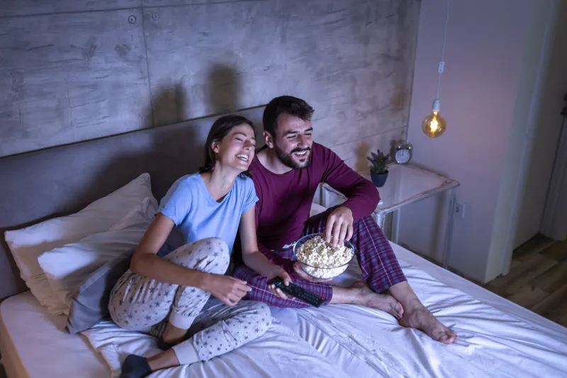 couple in love lying in bed, eating popcorn and watching a movie, relaxing at home at night