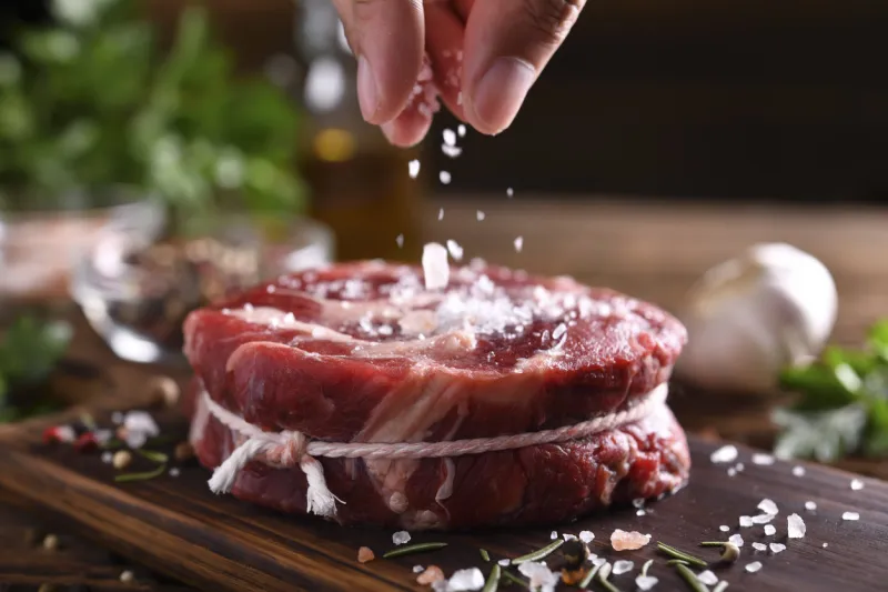 hand sprinkling salt on fresh raw beef meat on a cutting board