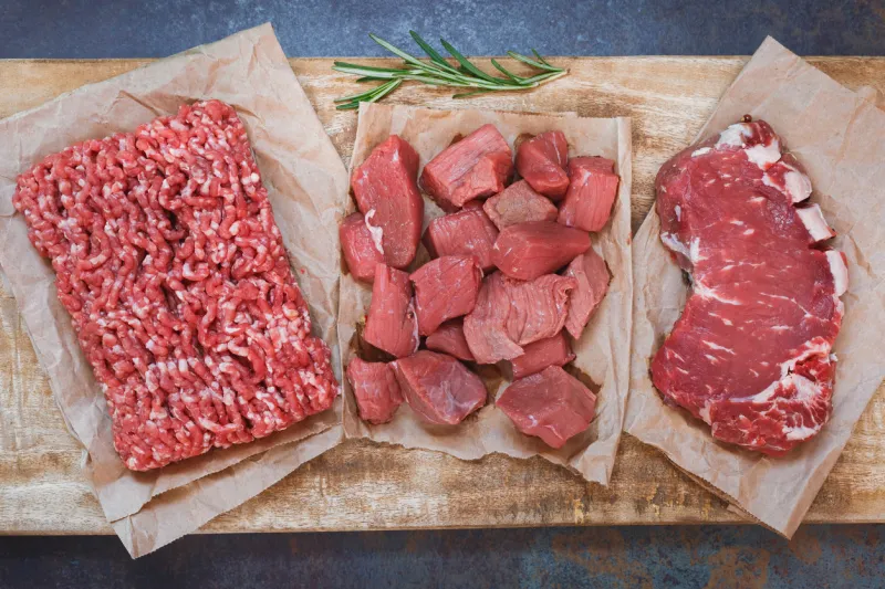 fresh raw angus beef meat, whole, ground and chopped on parchment paper , wooden cutting board, stone background, top view