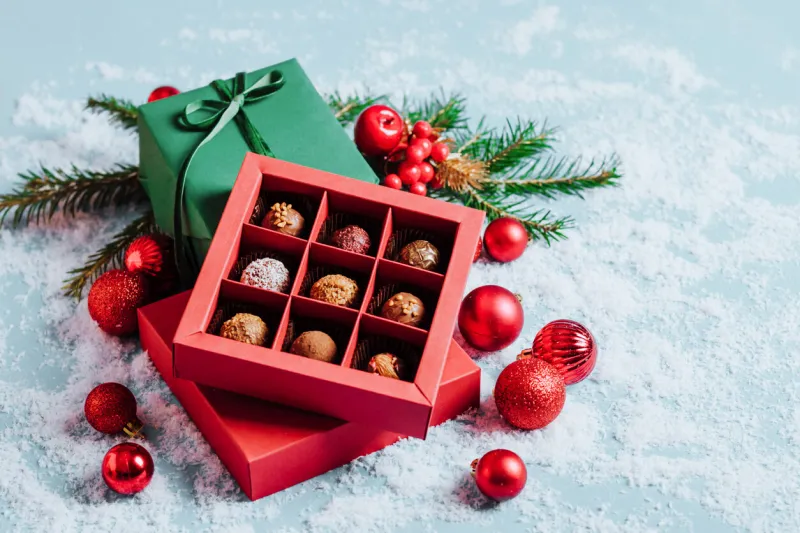 chocolates in a red festive box dark chocolate truffle on a christmas background with new year's toys balls fir branches top view flat mock up copy space holiday concept