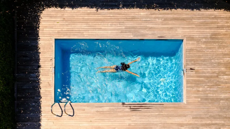 drone view full length of unrecognizable woman with long wet dark hair floating in outdoor swimming pool on sunny day in tropical resort