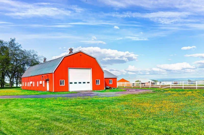 red orange painted barn shed with white doors in summer landscape field in countryside
