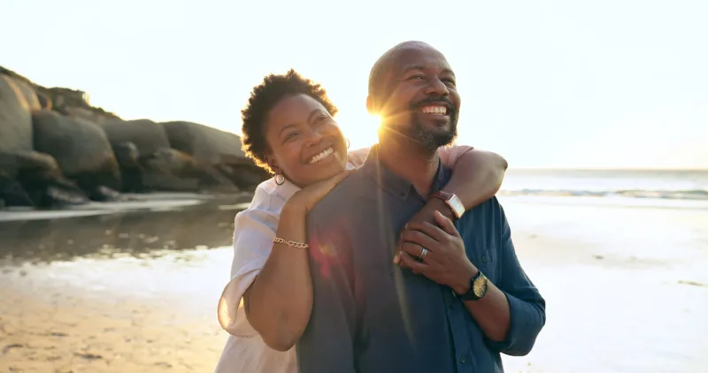couple, hug and happy on beach with love, bonding and sunset for holiday, vacation and relationship black people, man or woman with embrace, smile and romance by ocean or sea for travel or adventure