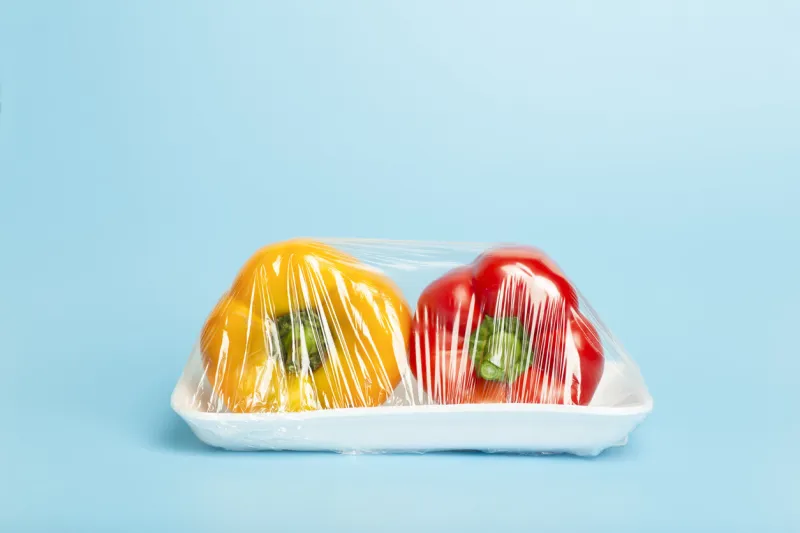 vegetables in plastic packaging from the supermarket are minimal pepper in cellophane and non-degradable plastic on a blue background biodegradable product packaging, environmental protection, nature pollution high quality photo