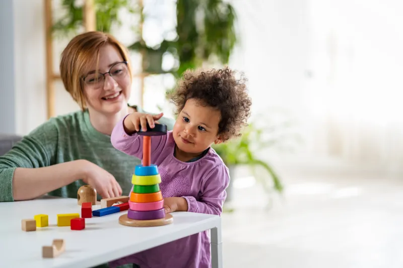 mother looking at a child playing with an educational didactic toy preschool teacher with a child playing with didactic toys mixed race family