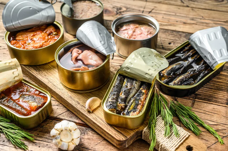 various canned fish and seafood in a metal cans wooden background top view