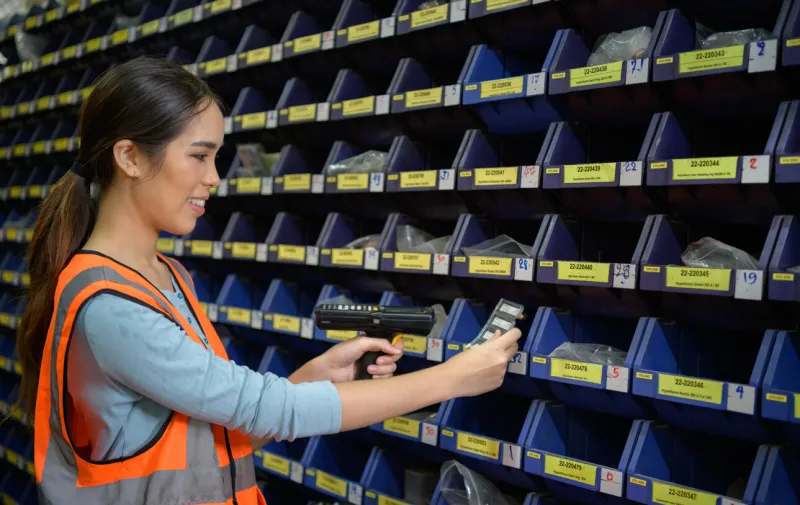 female warehouse worker counting small parts stored in the blue storage compartment to check the remaining amount in order to prepare for the next order