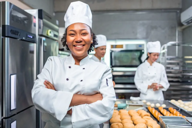 african american woman bakers looking at camerachef baker in a chef dress and hat, cooking together in kitchenshe takes fresh baked cookies out of modern electric oven in kitchen