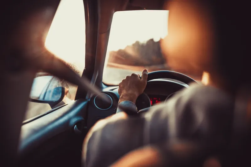 man driving car, hand on steering wheel, looking at the road ahead,sunset