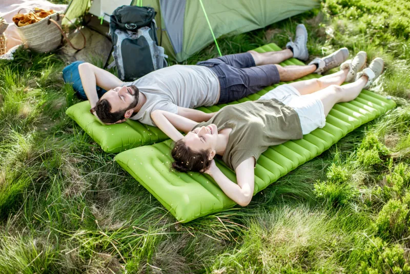 young and cheerful couple lying on the mattress at the campsite, enjoying summer time while traveling in the mountains
