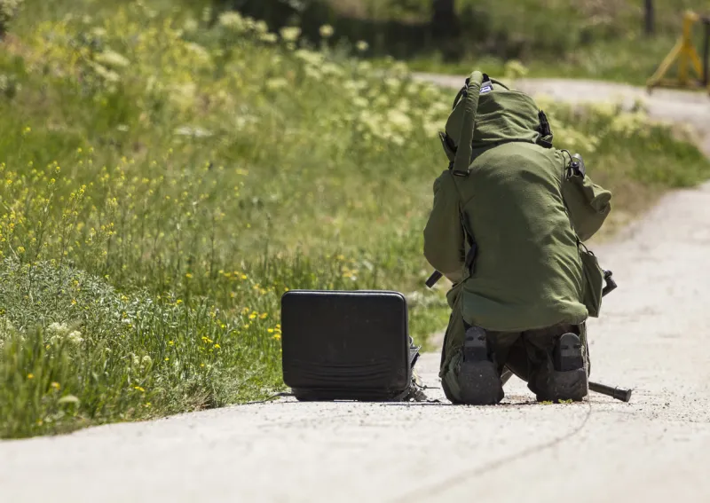 eod technician in bomb suit setting up a disrupter against a suspected bag