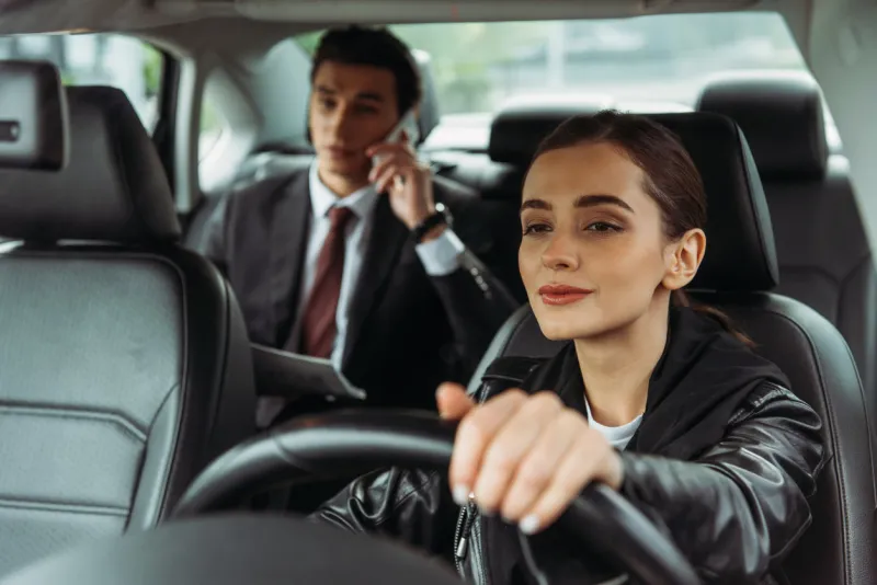 woman taxi driver holding steering wheel while businessman talking on smartphone